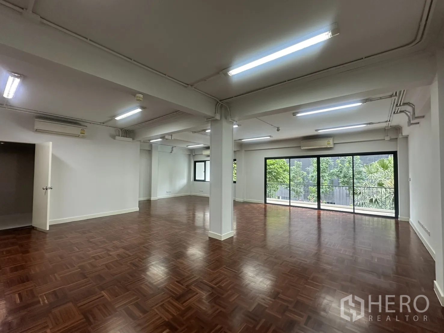 ออฟฟิศ for rent in Watthana, Bangkok - มุมกว้างของออฟฟิศพร้อมแอร์หลายเครื่อง เสาโครงสร้าง และวิวต้นไม้ผ่านหน้าต่างบานใหญ่