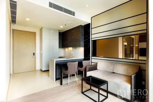 Condominium for rent or sale in Watthana, Bangkok - Open-plan living room with compact kitchen, dining for two and sofa in modern Asok condo.