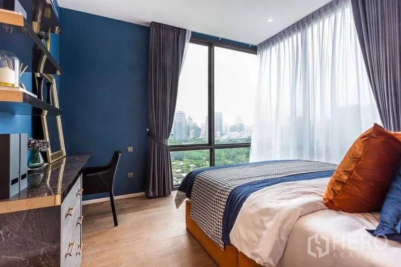 Condominium for rent in Pathum Wan, Bangkok - Bedroom with blue accent wall, large windows and park view.
