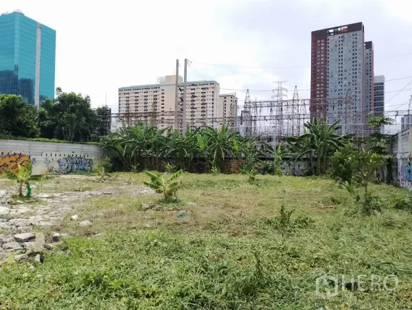 ที่ดิน ขายในSuan Luang, Bangkok - พื้นที่โล่งมีหญ้า กำแพงกราฟฟิตี พื้นหลังเป็นอาคารเมืองและโครงสร้างไฟฟ้า