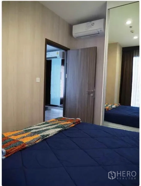 Condominium for rent in Huai Khwang, Bangkok - Second bedroom with air conditioning, blue bedding and full-height mirrored wardrobe.