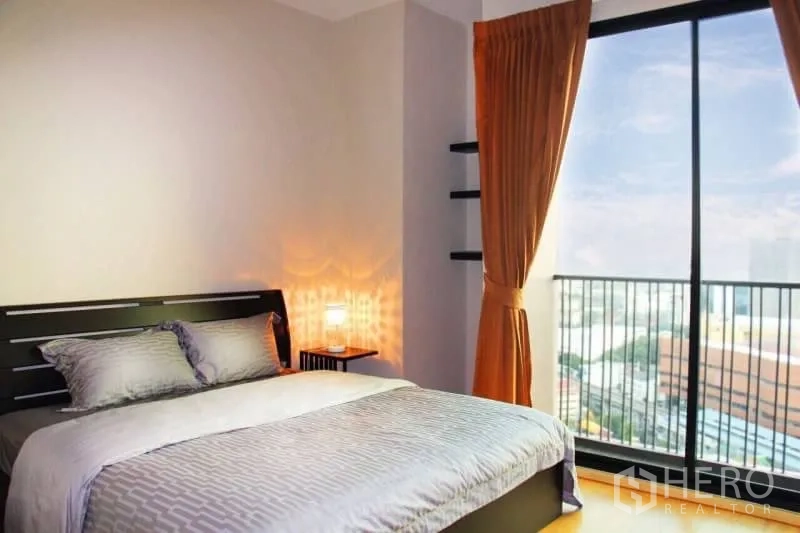 Condominium for rent or sale in Watthana, Bangkok - Cozy bedroom with double bed, warm lighting and floor‑to‑ceiling window city view.