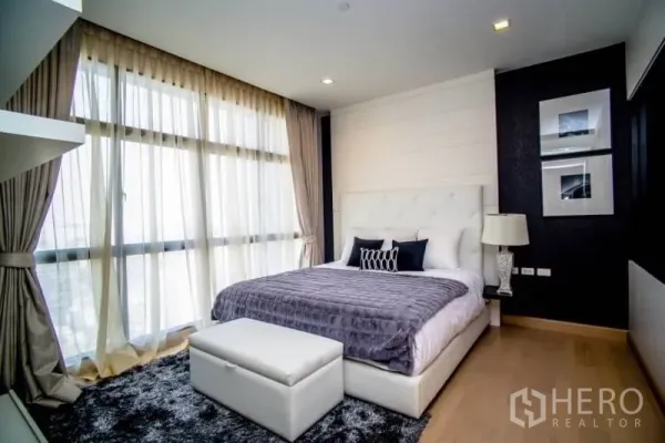 Condominium for rent in Khlong San, Bangkok - Bright master bedroom with floor-to-ceiling windows, tufted headboard and bedside lamps overlooking the city.