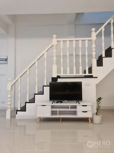 ทาวน์เฮาส์ ให้เช่าในKhlong Toei, Bangkok - บันไดราวลูกกรงสีขาว พร้อมชั้นวางทีวีและกระถางต้นไม้ด้านล่าง ในทาวน์เฮ้าส์สมัยใหม่