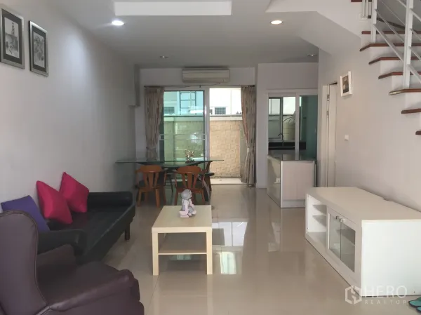 Townhouse for rent in Bang Kho Laem, Bangkok - Open-plan lounge and dining zone with staircase and a separate kitchen behind a glass partition.