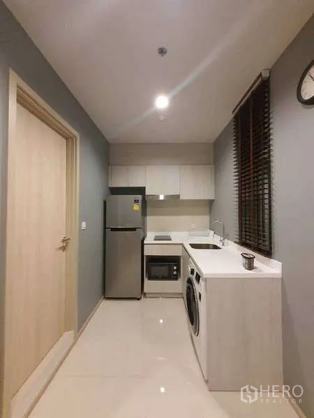 Condominium for rent - Compact kitchen with fridge, cooktop, microwave, sink, and washing machine.