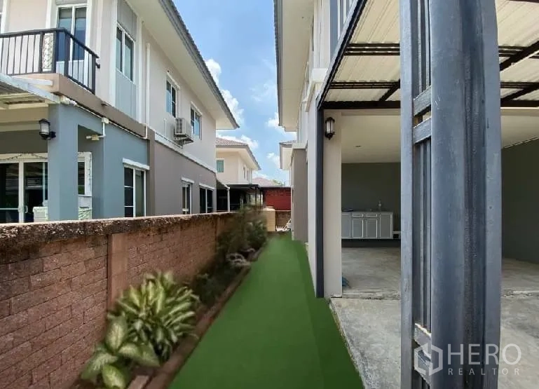 บ้าน ให้เช่าในSuan Luang, Bangkok - ทางเดินข้างบ้านปูหญ้าเทียมและไม้ประดับ ติดกับพื้นที่จอดรถมีหลังคาและเคาน์เตอร์ซักล้าง