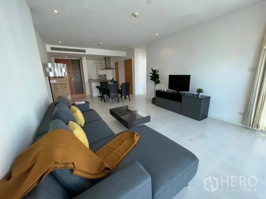 คอนโด ให้เช่าหรือขายในWatthana, Bangkok - ห้องนั่งเล่นกว้างแบบโอเพ่น มีโซฟาเข้ามุมสีเทา ตู้วางทีวี ชุดรับประทานอาหาร และครัวเปิด