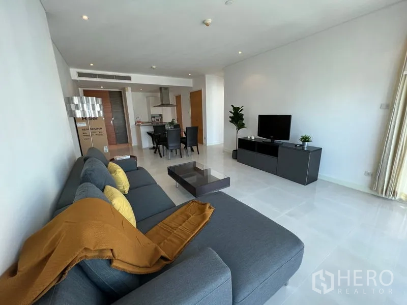 คอนโด ให้เช่าหรือขายในWatthana, Bangkok - ห้องนั่งเล่นกว้างแบบโอเพ่น มีโซฟาเข้ามุมสีเทา ตู้วางทีวี ชุดรับประทานอาหาร และครัวเปิด