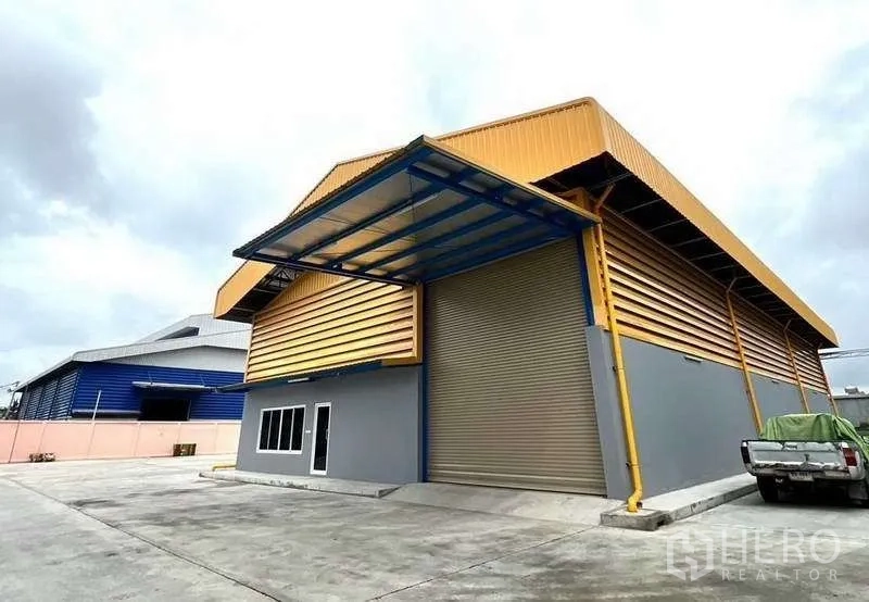Warehouse for rent in Lat Lum Kaeo, Pathum Thani - Main entrance of warehouse with roll-up shutter and blue canopy beside a pickup.