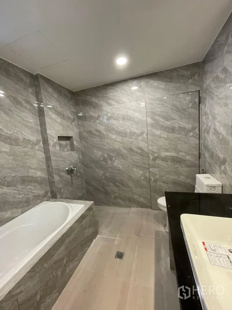 คอนโด ให้เช่าในKhlong Toei, Bangkok - ห้องน้ำสมัยใหม่ ผนังลายหินอ่อนสีเทา อ่างอาบน้ำ และเคาน์เตอร์หินสีดำ