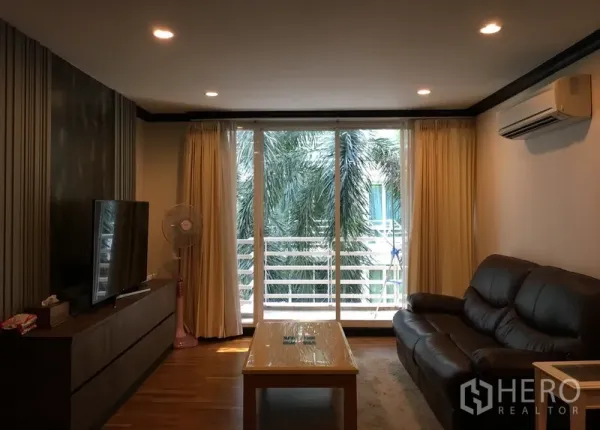 คอนโด ขายในKhlong Toei, Bangkok - ห้องนั่งเล่นสว่าง โซฟาหนัง ตู้ทีวี และประตูกระจกเปิดสู่ระเบียงวิวต้นปาล์ม