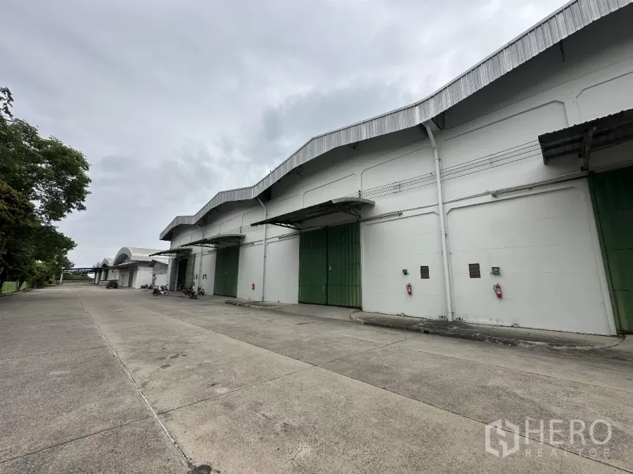 货栈 出租在Bang Pa-in, Phra Nakhon Si Ayutthaya - 安全园区内一排白色仓库，绿色装卸门与宽阔混凝土通道。