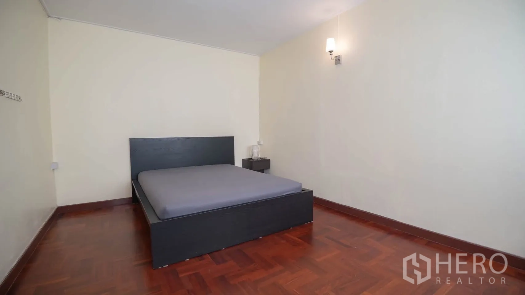 Townhouse for rent in Watthana, Bangkok - Minimal bedroom with dark bed frame, bedside table, and parquet floor.