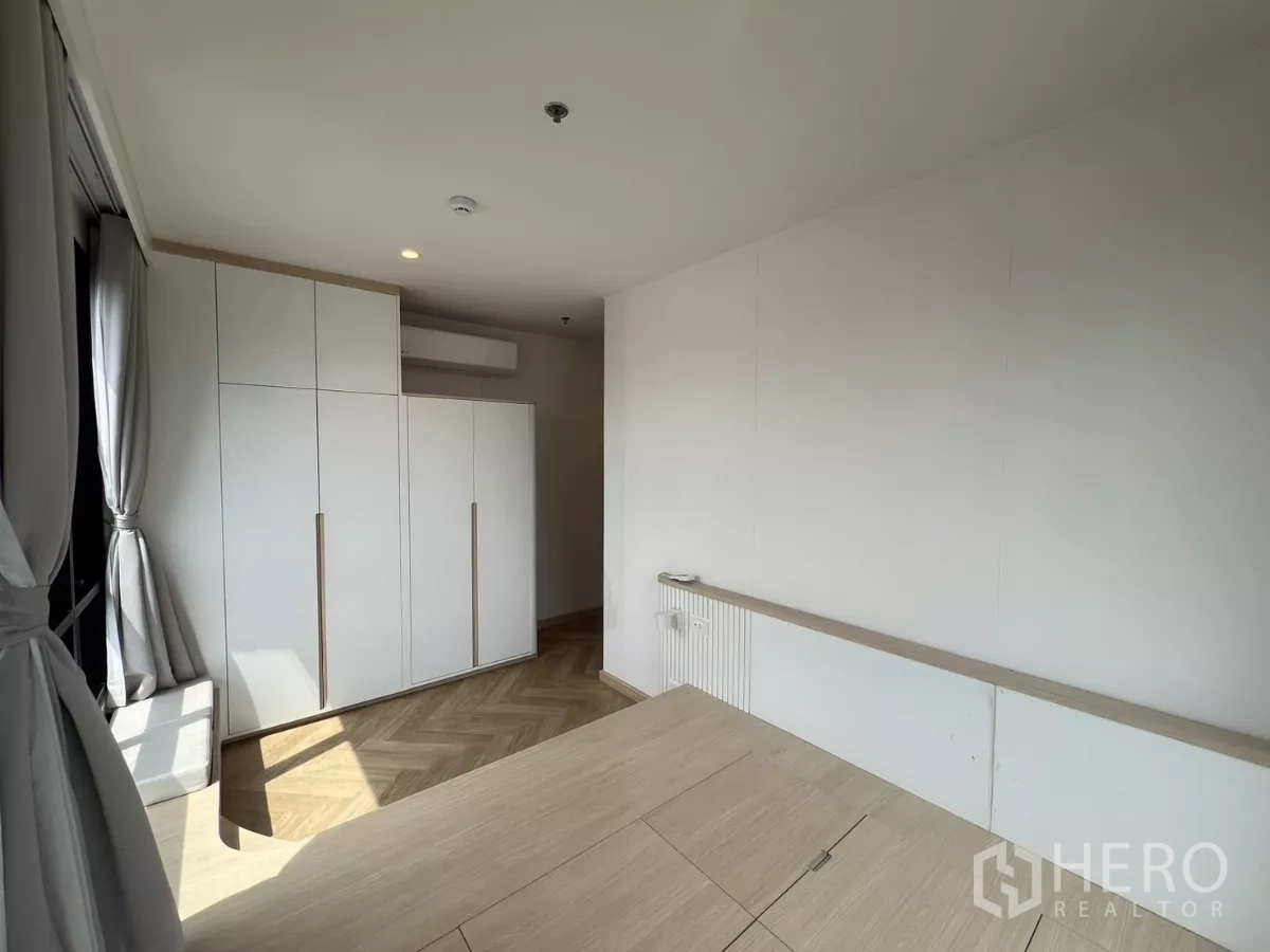 Condominium for rent or sale in Chatuchak, Bangkok - Bedroom angle showing wardrobe and raised platform bed with curtain‑framed windows.