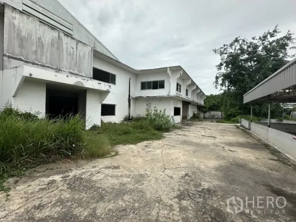 Factory for rent or sale in Khlong Luang, Pathum Thani - Side driveway beside the factory block with overgrown greenery and service access.