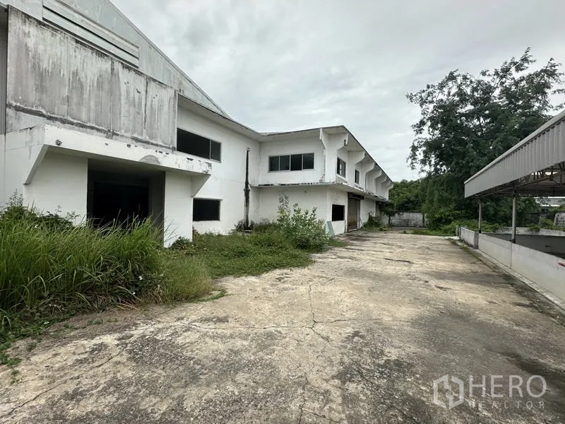 Factory for rent or sale in Khlong Luang, Pathum Thani - Side driveway beside the factory block with overgrown greenery and service access.