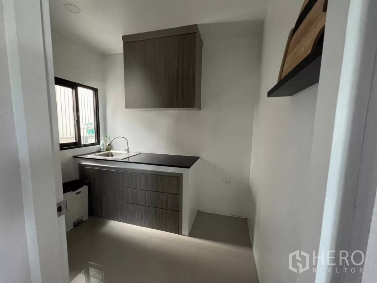 Detached House for rent in Samut Prakan - Separate kitchen with window, dark wood cabinets, black countertop and stainless sink.