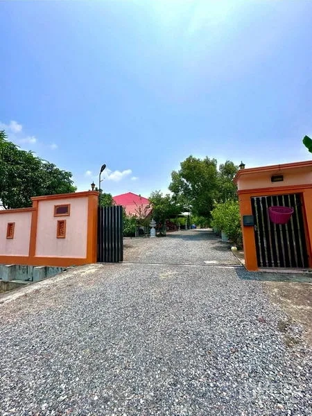 Detached House for sale in Bang Bua Thong, Nonthaburi - Gated entrance with orange walls and a wide gravel driveway leading toward the house.