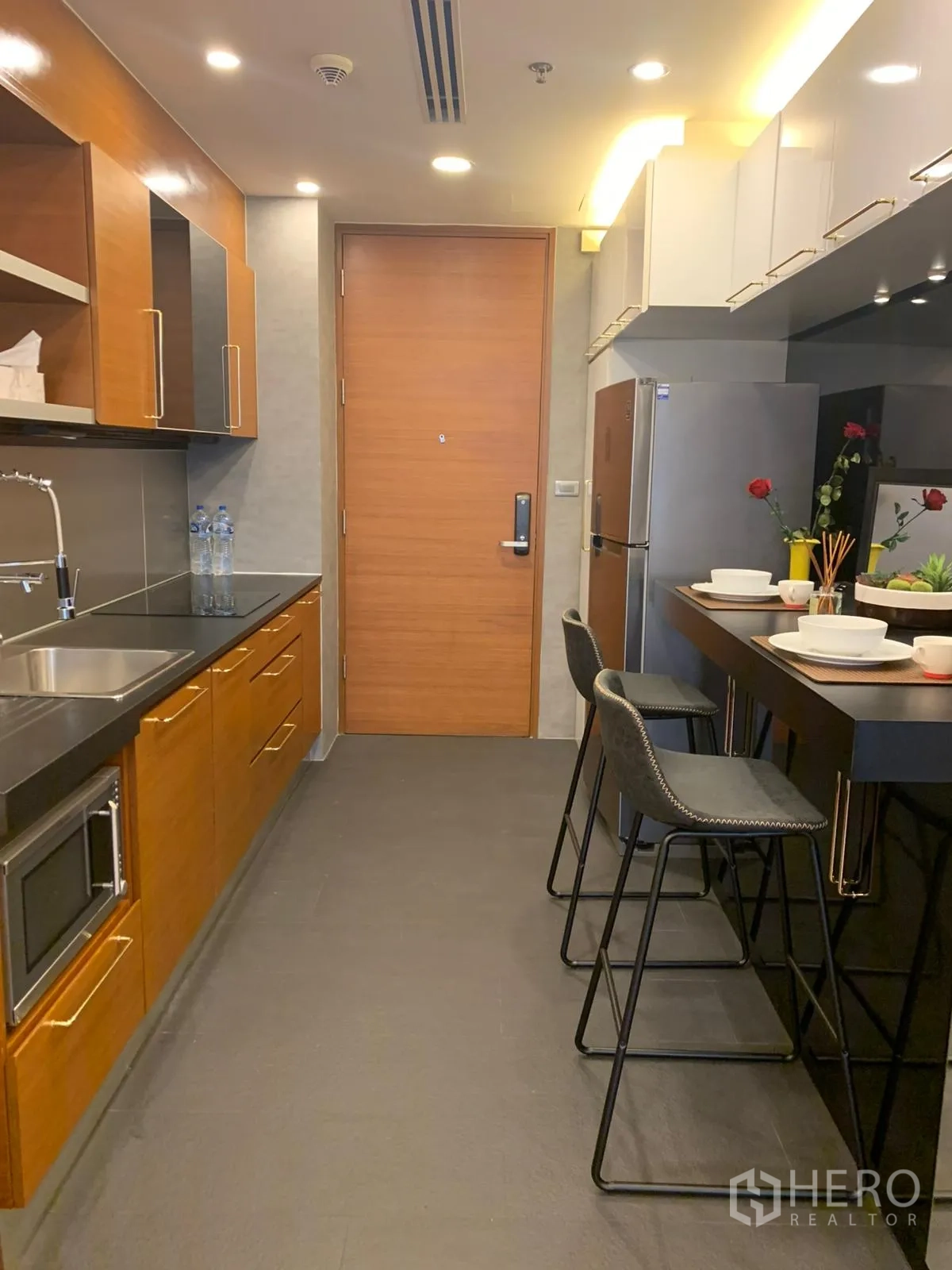 公寓 出售在Khlong Toei, Bangkok - 现代长廊式厨房，木质橱柜、吧台与不锈钢冰箱。