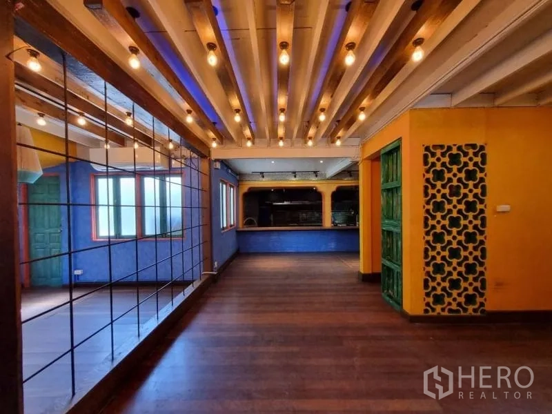 Detached House for rent in Khlong Toei, Bangkok - Open-plan hall with wood beams, mirror wall and warm pendant bulbs.