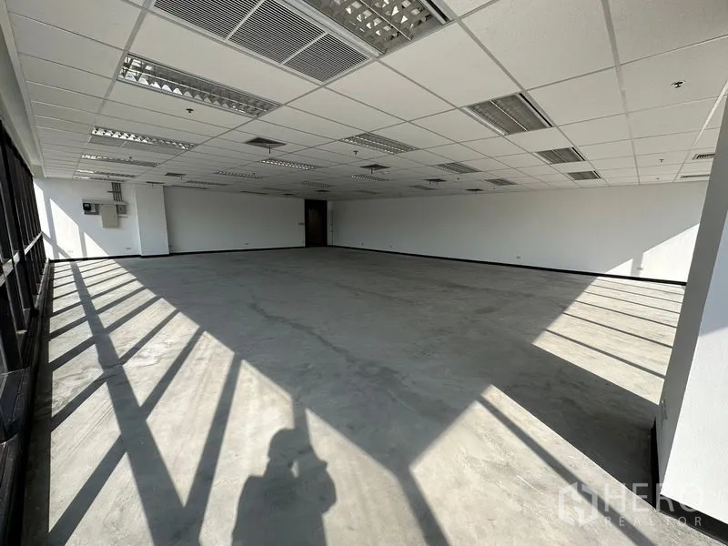 Office Space for rent in Watthana, Bangkok - Large unfurnished office with a long wall of windows casting daylight shadows.