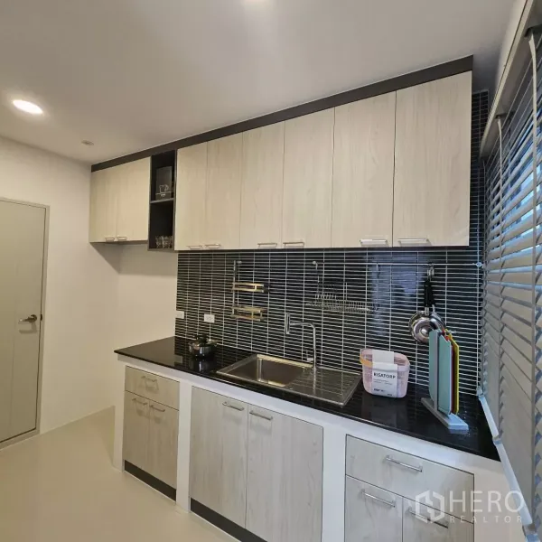 Detached House for rent in Bang Phli, Samut Prakan - Modern kitchen with light wood cabinetry, black stone countertop and slim tile backsplash beside a window.