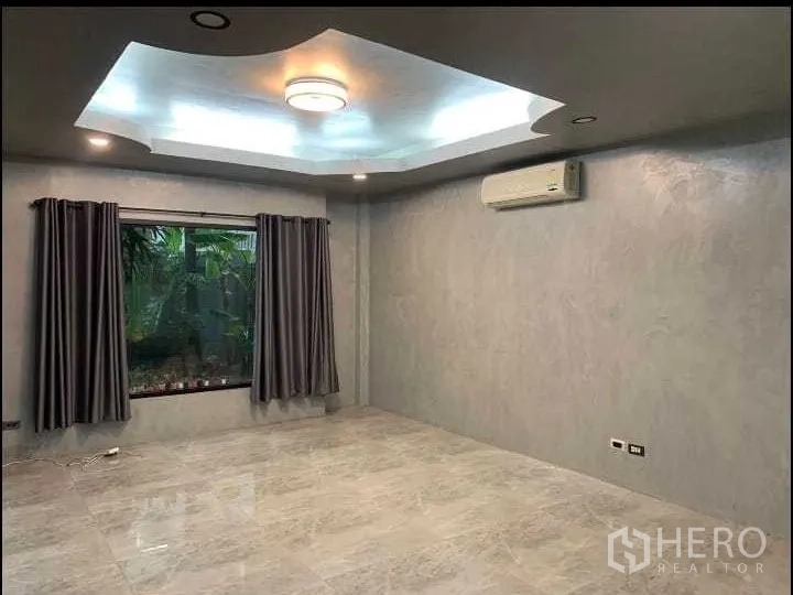 Detached House for rent or sale in Wang Thonglang, Bangkok - Bright living room with tray ceiling lighting, large window with curtains and wall-mounted air conditioner.