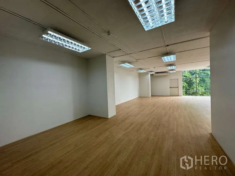 Office Space for rent in Sathon, Bangkok - Long view of open workspace with column, wood flooring, multiple ceiling lights and full-height windows to trees.