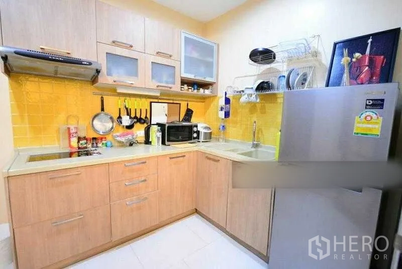 Condominium for rent in Bang Kho Laem, Bangkok - U-shaped kitchen with light wood cabinetry, yellow backsplash and full appliances.