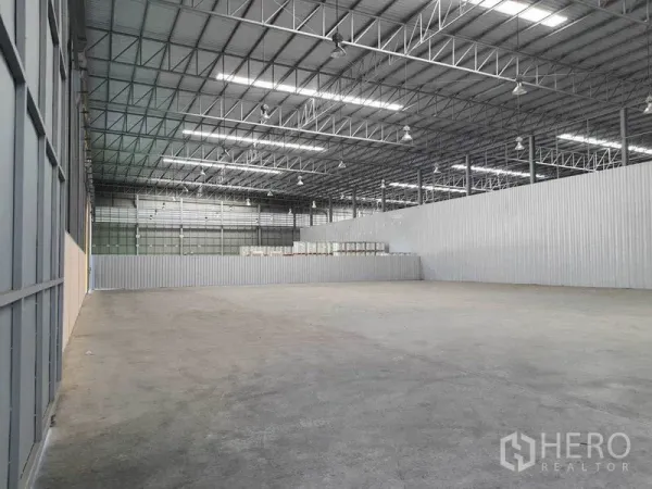 Warehouse for rent in Chachoengsao - Open storage bay separated by corrugated metal partition under LED high-bay lighting.