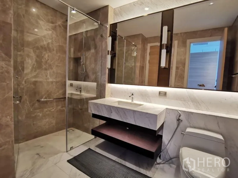 Condominium for rent in Pathum Wan, Bangkok - Luxury bathroom with glass shower, marble vanity and backlit mirrors.
