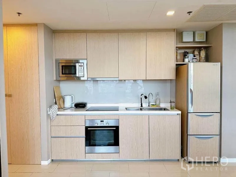 Condominium for rent in Ratchathewi, Bangkok - Light wood built-in kitchen with oven, cooktop, microwave, and full-size refrigerator.