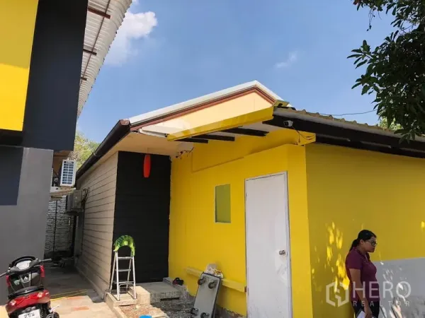 บ้าน ขายในKhlong Toei, Bangkok - อาคารชั้นเดียวต่อเติม สีเหลือง ประตูสีขาว มีกันสาดเหล็ก ข้างตัวบ้าน