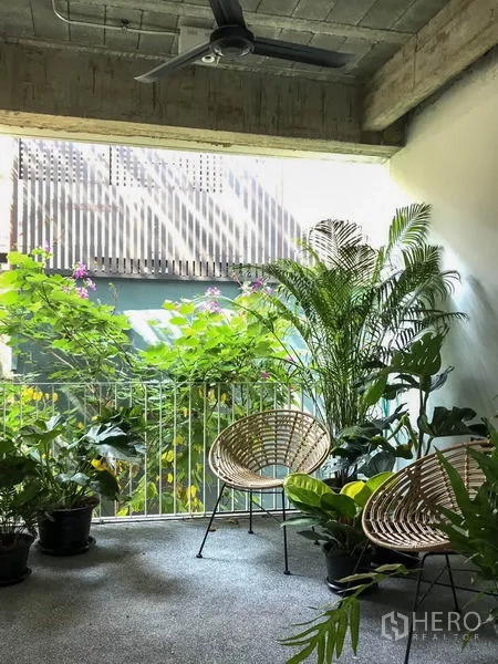 Townhouse for rent in Khlong Toei, Bangkok - Covered balcony with ceiling fan, potted tropical plants and woven chairs.