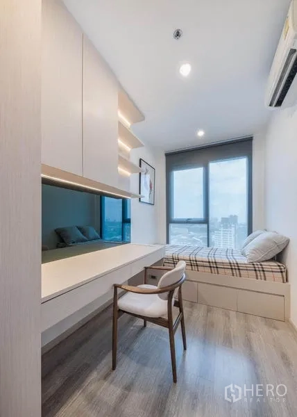 Condominium for rent in Bang Na, Bangkok - Study or guest room with long built-in desk, chair, and single bed by the window.