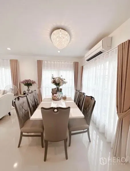 Detached House for rent in Bueng Kum, Bangkok - Sunlit dining space for six with neutral décor, floor-to-ceiling curtains and AC unit.