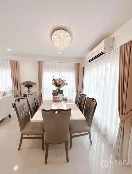Detached House for rent in Bueng Kum, Bangkok - Sunlit dining space for six with neutral décor, floor-to-ceiling curtains and AC unit.