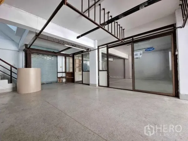 办公空间 出租在Din Daeng, Bangkok - 宽敞开放式办公室，带玻璃隔断、外露金属梁、卷帘门和水泥地面。