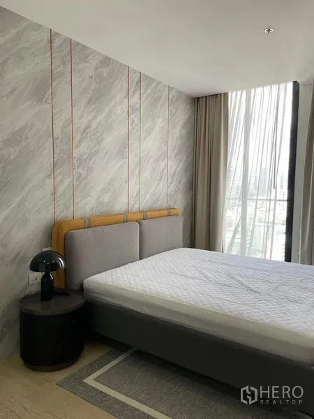 Condominium for rent in Pathum Wan, Bangkok - Bright bedroom with gray headboard, marble accent wall and floor-to-ceiling windows.