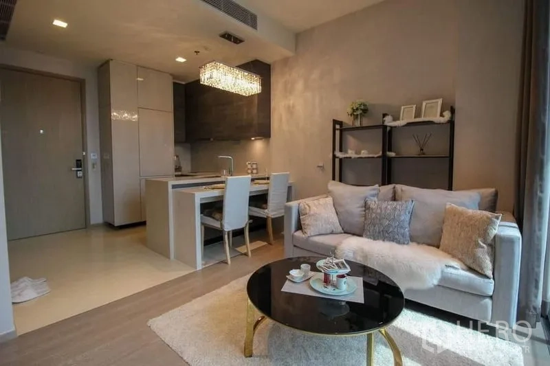 Condominium for sale in Watthana, Bangkok - Open-plan living and dining with a grey sofa, round black coffee table and crystal chandelier above the island kitchen.