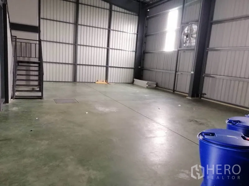 Warehouse for rent or sale in Lam Luk Ka, Pathum Thani - Spacious warehouse interior with high ceiling, steel-clad walls, ventilation fan, and heavy-duty concrete floor.