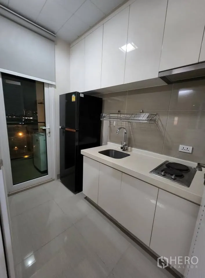 Condominium for rent in Huai Khwang, Bangkok - Modern galley kitchen with white cabinets, XL fridge and electric cooktop.