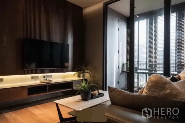 公寓 出租在Khlong Toei, Bangkok - 电视背景墙带木质竖纹与灯带，旁侧为通向阳台/日光区的玻璃门。