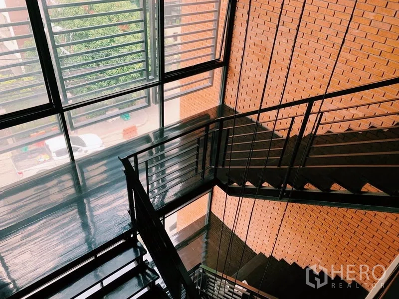 คอนโด ให้เช่าในWatthana, Bangkok - โถงบันไดสว่างด้วยแสงธรรมชาติ บันไดเหล็กสีดำ ผนังอิฐ และหน้าต่างบานเกล็ดสูงจรดเพดาน