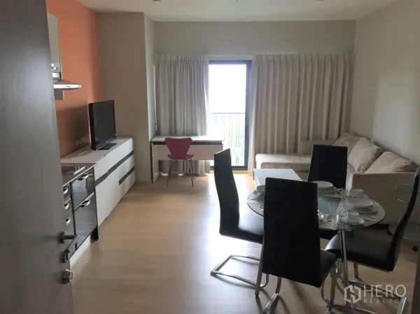 Condominium for rent in Watthana, Bangkok - Open-plan living and dining room with kitchenette, glass dining table, sofa and balcony doors.