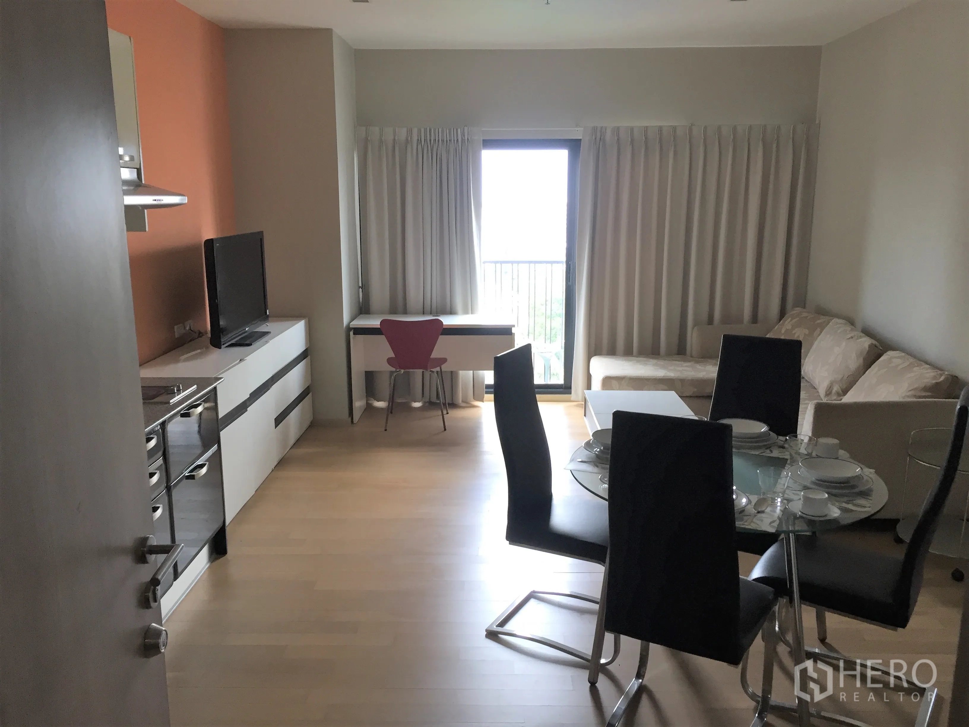 Condominium for rent in Watthana, Bangkok - Open-plan living and dining room with kitchenette, glass dining table, sofa and balcony doors.
