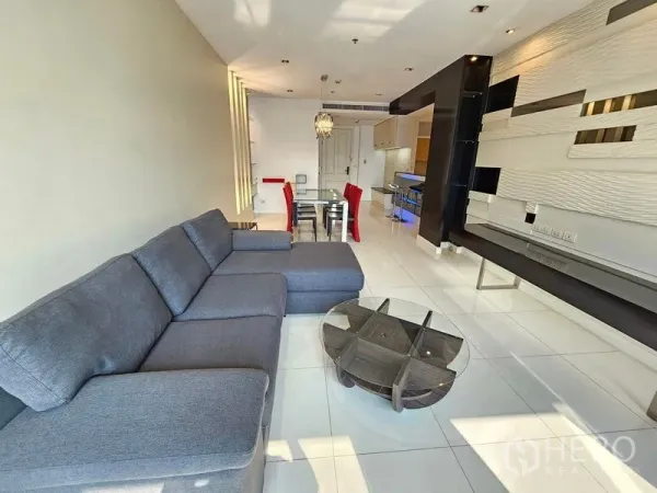 Condominium for rent or sale in Pathum Wan, Bangkok - Open-plan living and dining area with grey sectional sofa, glass coffee table and modern wall paneling.