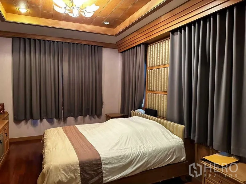 Detached House for sale in Bang Khun Thian, Bangkok - Warm bedroom with tray ceiling, wooden floor and full-length curtains around a double bed.