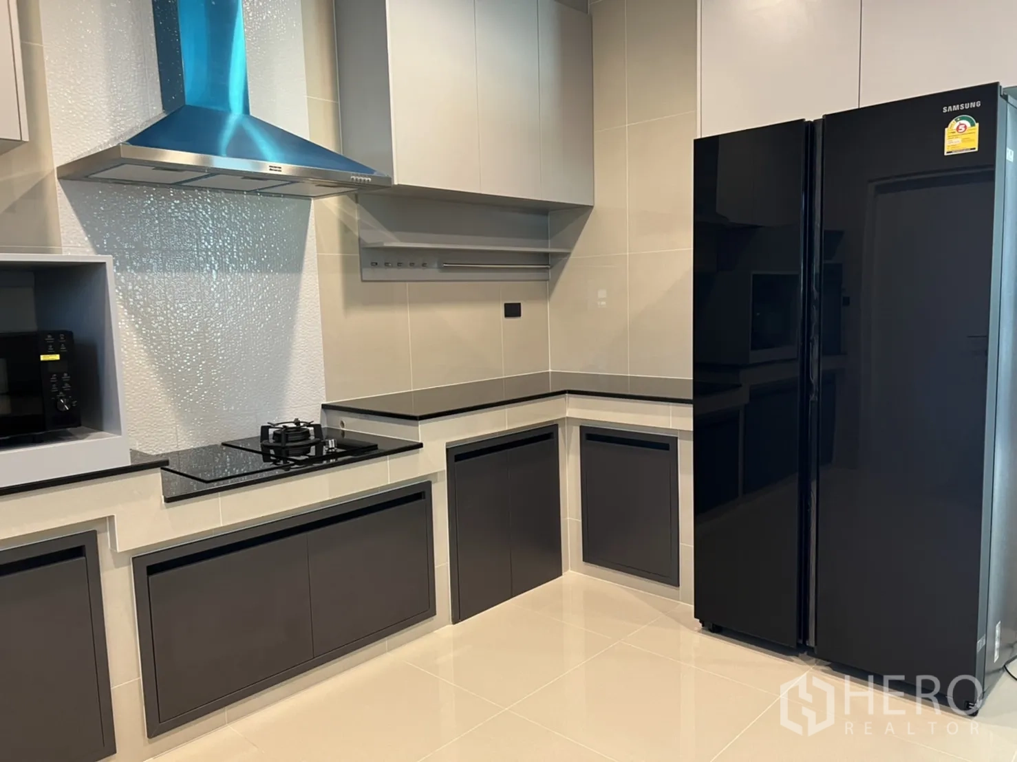 Detached House for rent in Bang Kapi, Bangkok - Modern kitchen with glossy cabinetry, black countertops, gas hob, hood, and a large fridge.